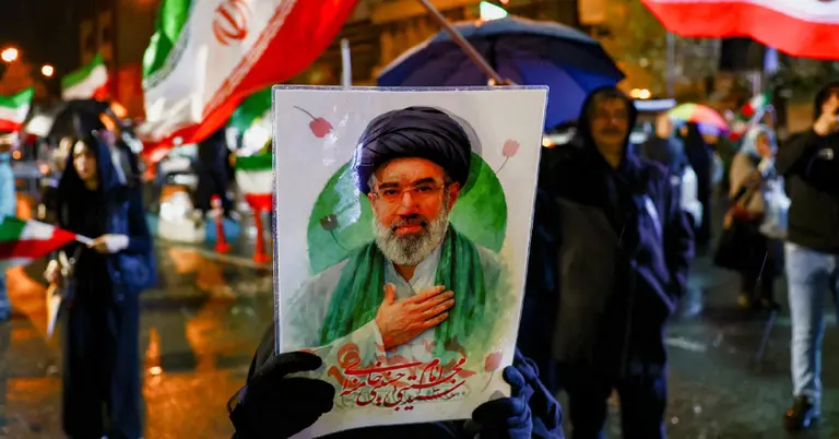 তেহরানের রাস্তায় এক নারী মুজতবা খামেনি পোস্টারের হাতে দাঁড়ানো